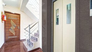 A hallway with a wooden door, a fire extinguisher, a staircase, and a modern wall with windows.