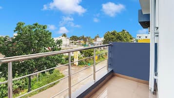 Een balkon met een metalen hekwerk, uitzicht op een woongebied met bomen en gebouwen.