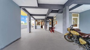 A covered outdoor area with a motorcycle parked, a table with chairs, and a view of buildings in the background.