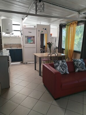 Ein kompakter Wohnbereich mit Küchenzeile, Essplatz und einem roten Sofa mit gemusterten Kissen.