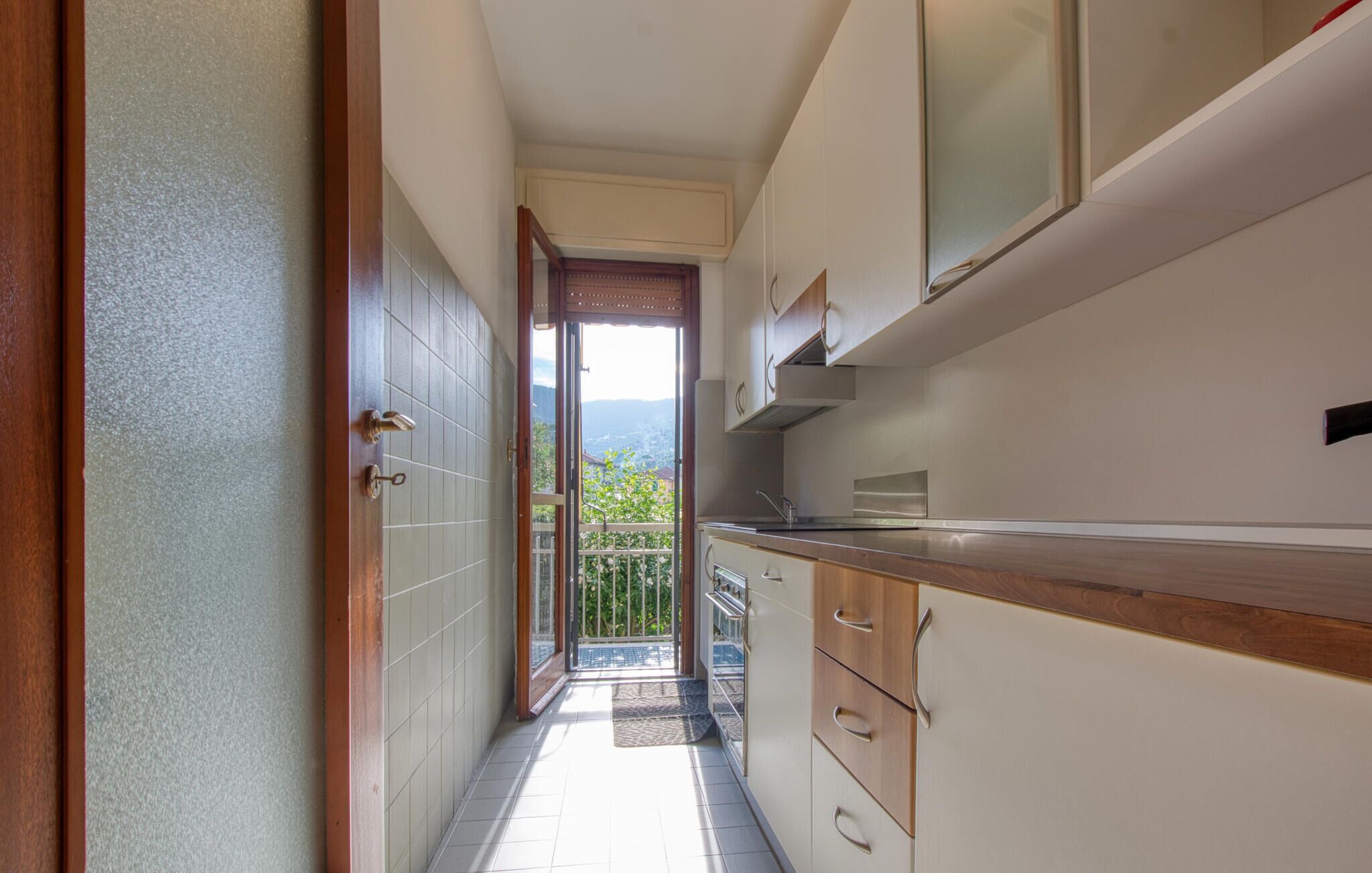 Una cucina stretta con mobili in legno, un lavello in acciaio inossidabile e vista su un balcone con una porta che dà sull'esterno.