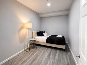 A bedroom with a bed, bedside table, lamp, and a door.