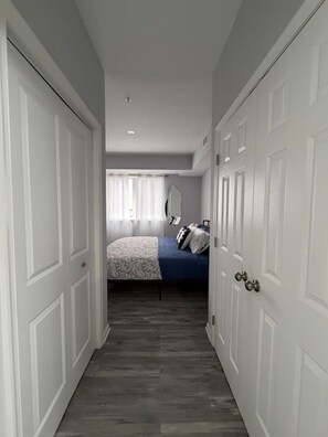 A narrow hallway leading to a bedroom with a bed, a mirror, and a wardrobe.