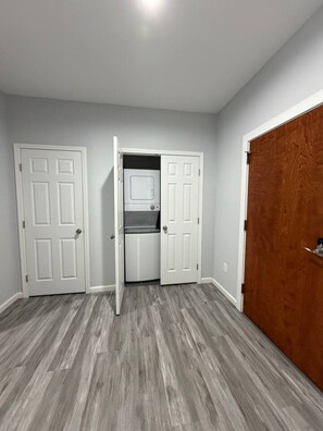 A hallway with two white doors, one leading to a laundry room with a washer and dryer, and another to a wooden closet.