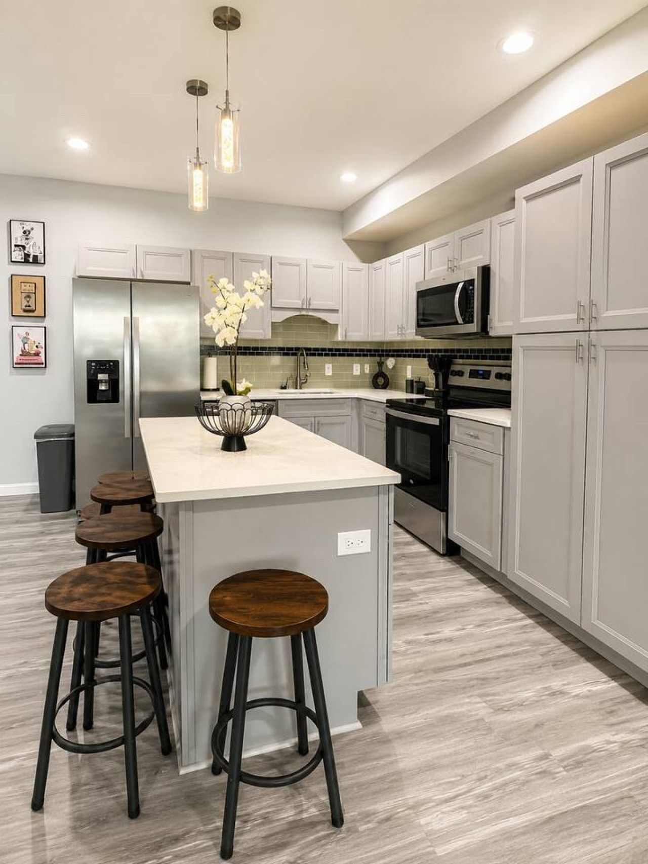 A modern kitchen with a central island, bar stools, stainless steel appliances, and a tiled backsplash.