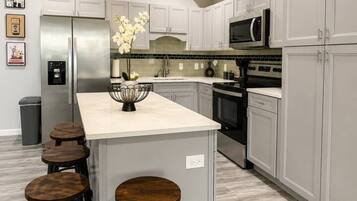 A modern kitchen with a central island, bar stools, stainless steel appliances, and a tiled backsplash.