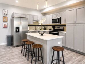 A modern kitchen with a central island, stainless steel appliances, and bar stools.