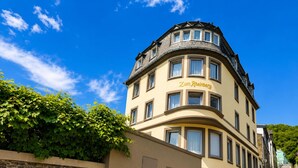 A building with a curved facade, multiple windows, and a stone wall with a sign. - Zum Rheinberg - City Studio (Braubach)