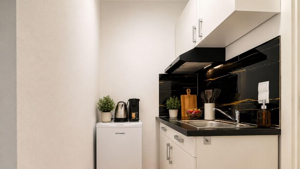 A compact kitchen with white cabinetry, a built-in dishwasher, a coffee maker, and a small potted plant. - Zum Rheinberg - City Studio (Braubach)