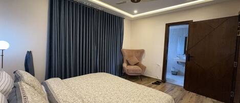 A bedroom with a bed, a chair, a ceiling fan, and a door leading to a bathroom.