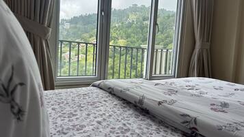 Une chambre à coucher avec un lit, des rideaux et un balcon donnant sur un paysage verdoyant.