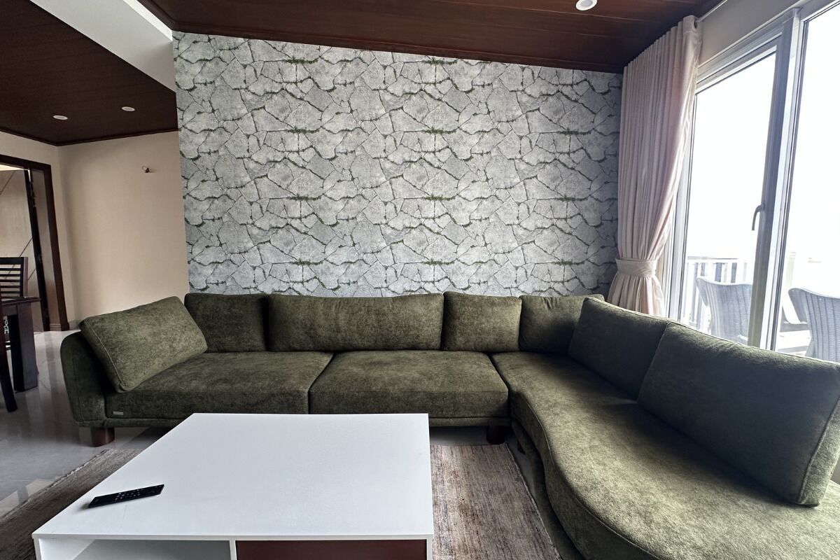 Sala de estar com sofá seccional, mesa de centro branca e parede com padrão de pedra.