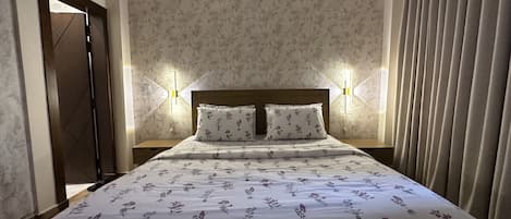 Une chambre d’hôtel avec un lit, une literie à motifs floraux, deux lampes de chevet et une porte.