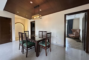 Un comedor con mesa y sillas de madera, una araña y vista a otra habitación con una silla.