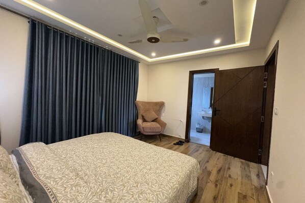 A bedroom with a bed, a chair, a ceiling fan, and a door leading to a bathroom.