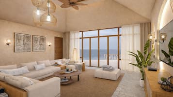 Un salón espacioso con un gran ventanal con vistas al mar, un ventilador de techo y una zona de estar acogedora.