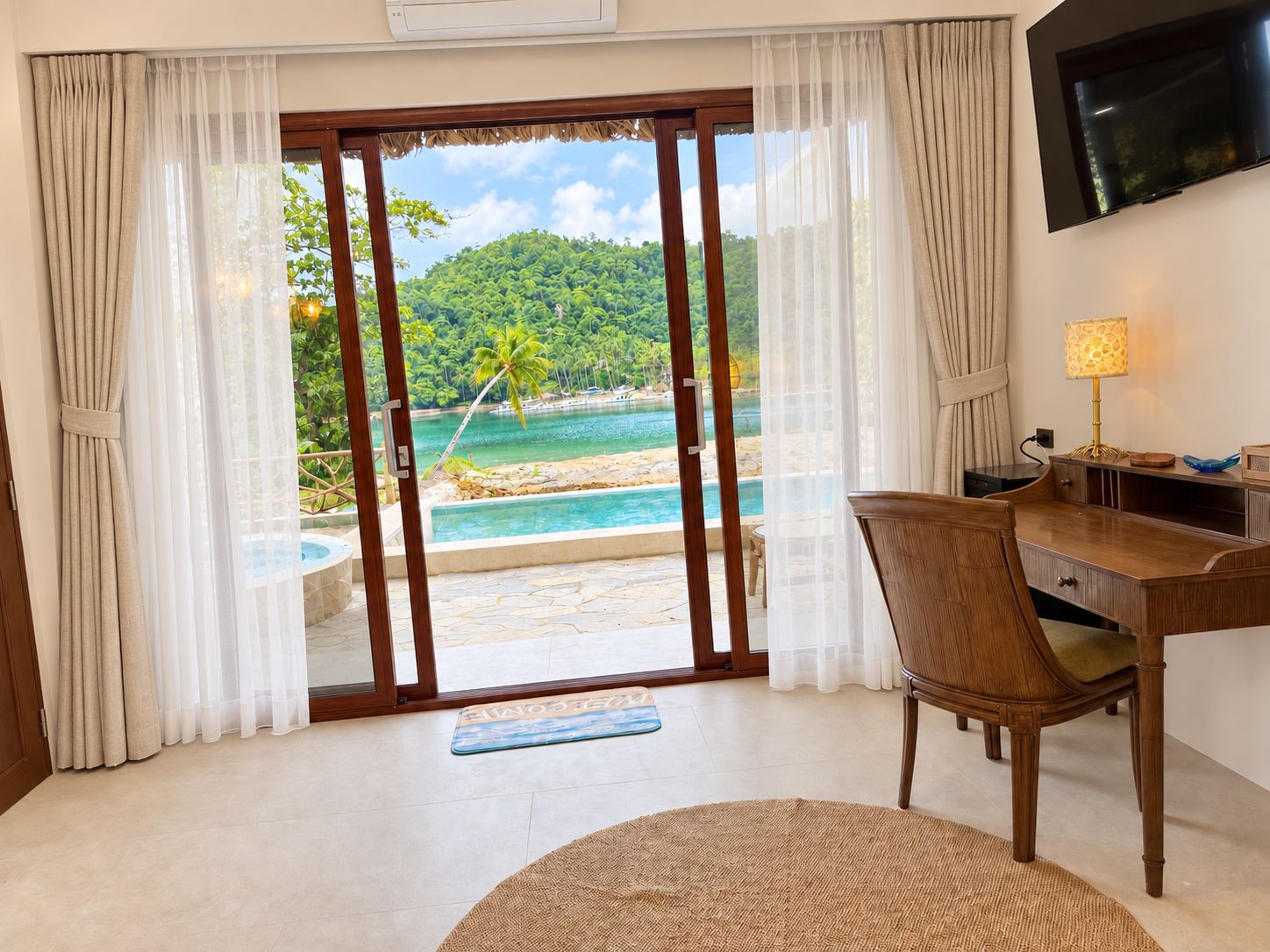 A room with a desk, chair, and a view of a pool and beach.