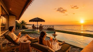 Un resort con piscina, sillas de descanso y vista al océano al atardecer.