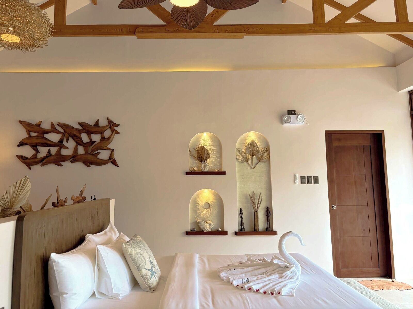 A hotel room with a bed, a wooden ceiling, wall art, and a door.