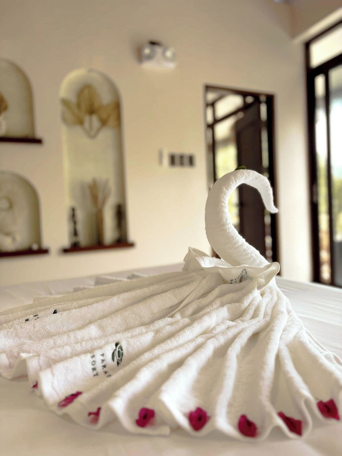 A neatly folded white towel with a swan design, placed on a bed in a hotel room.