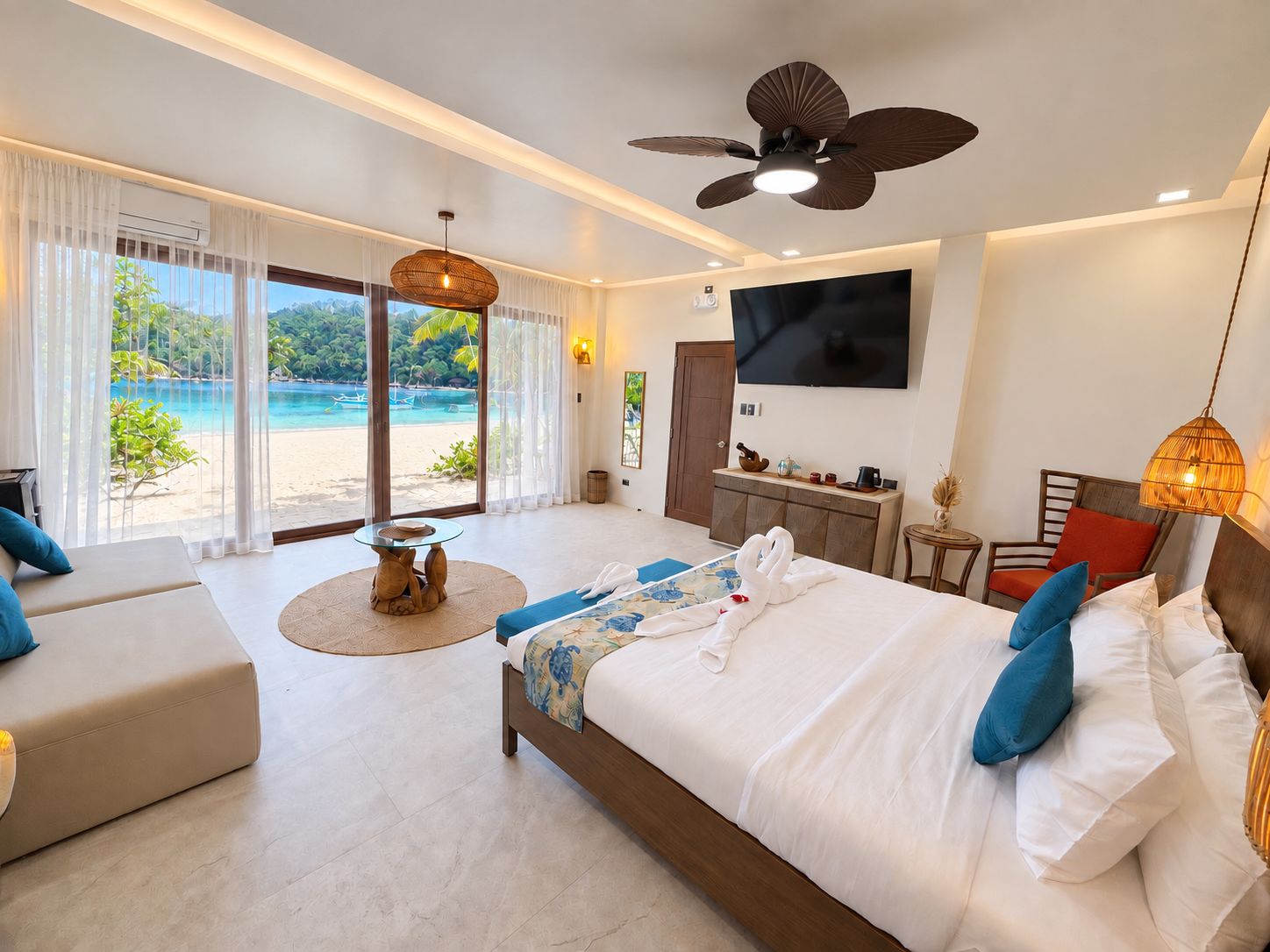 A hotel room with a bed, a sofa, a TV, and a view of a beach.