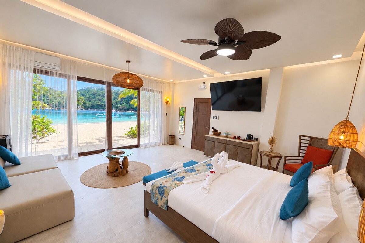 A hotel room with a bed, a sofa, a TV, and a view of a beach.
