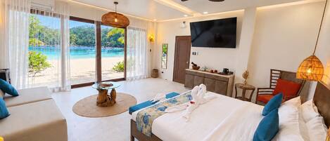A hotel room with a bed, a sofa, a TV, and a view of a beach.