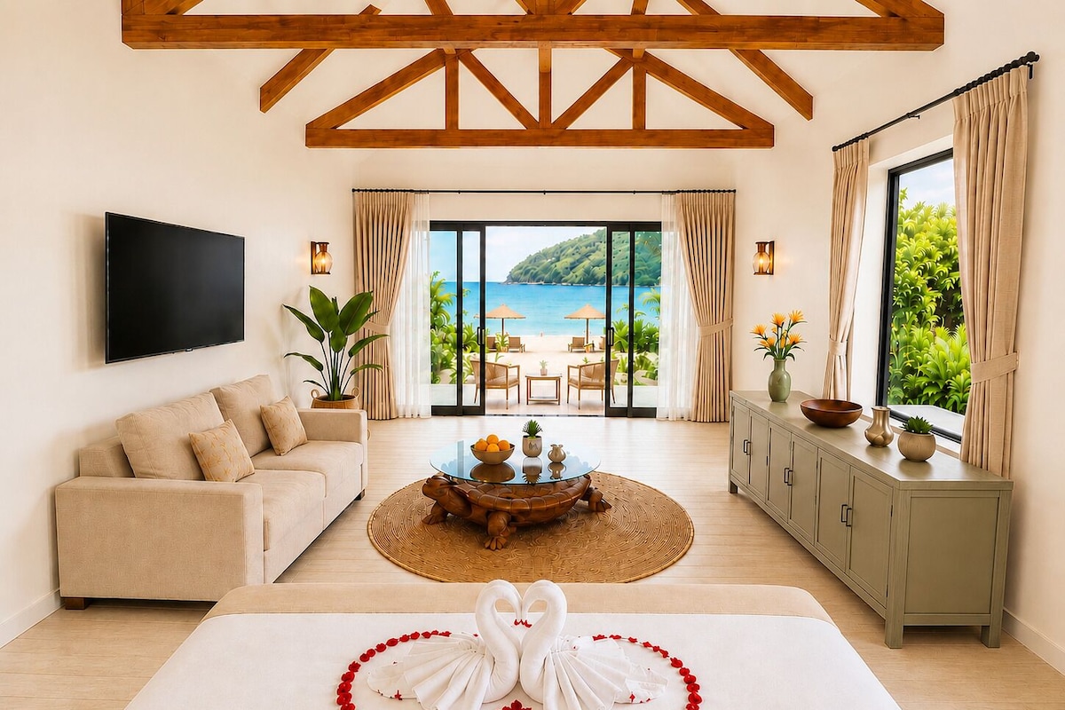 A hotel room with a large bed, a sofa, a TV, and a view of the beach.