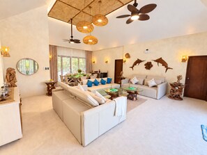 A spacious living area with a sofa set, a dining table, and a ceiling fan.