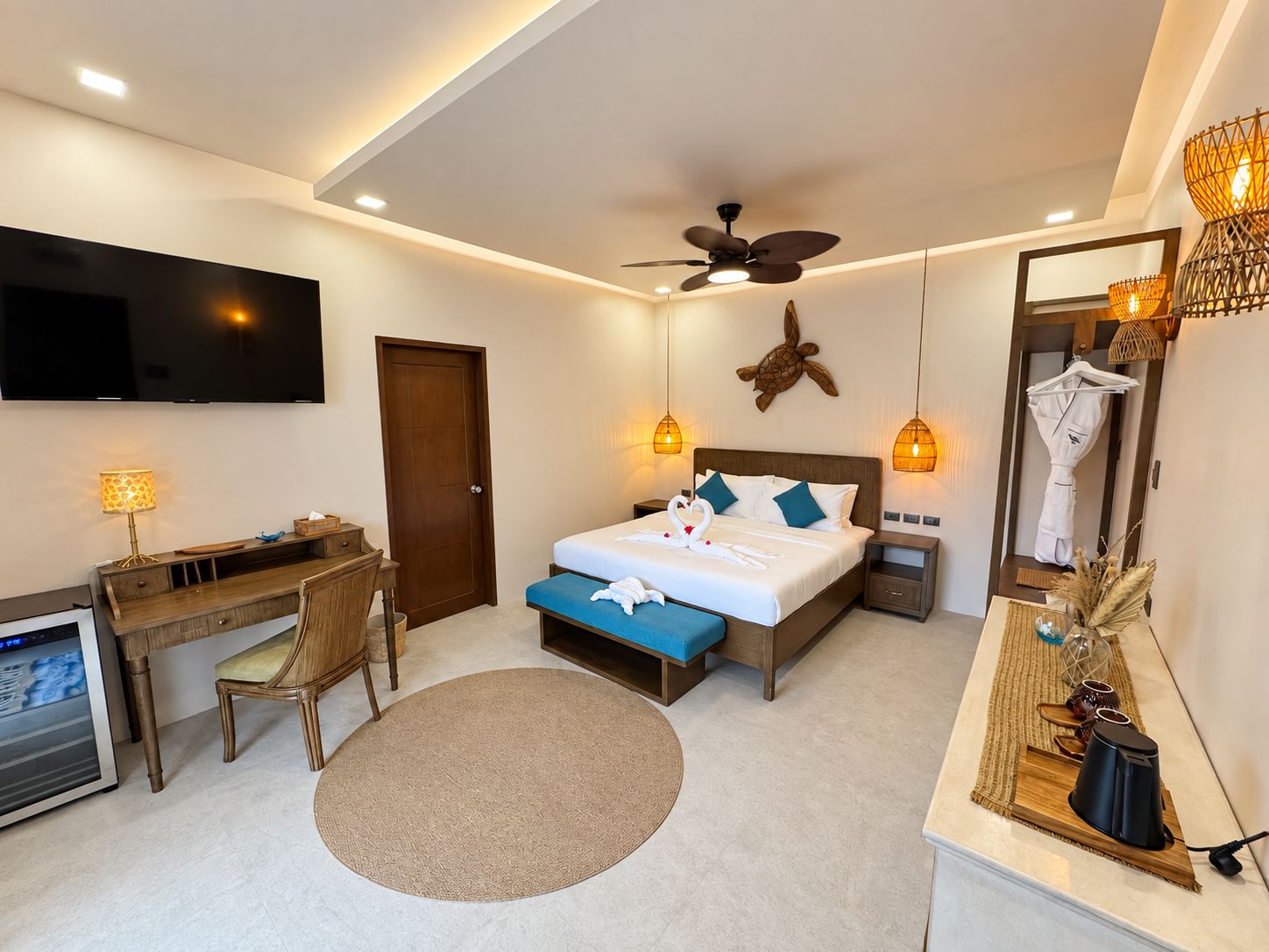 Ein Hotelzimmer mit Bett, Schreibtisch, Stuhl, Fernseher, Deckenventilator und Nachttischlampen.