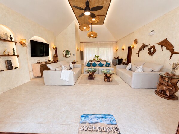 A spacious living room with a large flat-screen TV, two sofas, a coffee table, and a ceiling fan.