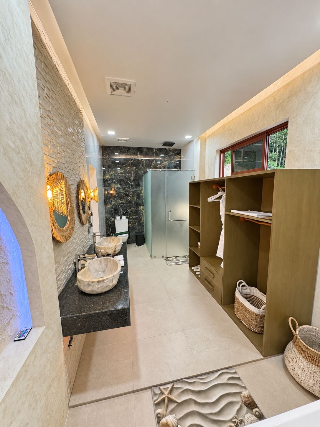 Une salle de bain moderne avec un meuble-lavabo en marbre, une douche en verre et des étagères en bois où sont rangées les serviettes.