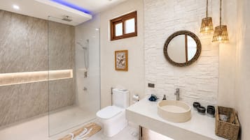 Un baño moderno con ducha envuelta en vidrio, inodoro, lavabo de diseño redondo y espejo con marco decorativo.