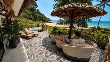 A beachside lounge with wicker furniture, a pool, and a view of the ocean.