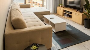 Uma sala de estar moderna com um sofá, uma mesa de centro, um rack para TV e vista para uma varanda.