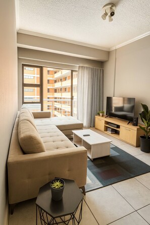 Una sala moderna con un sofá, una mesa de centro, un mueble para televisión y vistas a un balcón exterior.