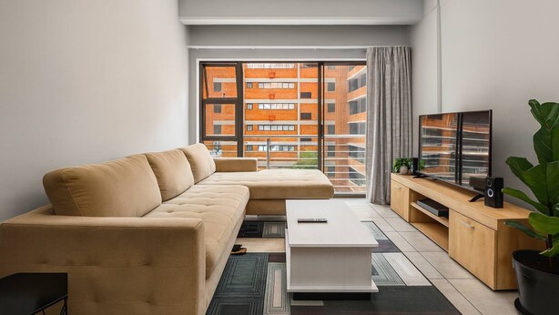 Een moderne woonkamer met een bank, salontafel, televisie en uitzicht op een gebouw van baksteen.