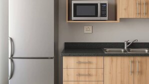 Een keuken met een roestvrijstalen koelkast, een magnetron, houten keukenkastjes, een aanrecht en een spoelbak.