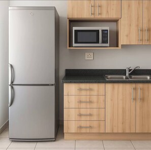 Eine Küche mit einem Edelstahlkühlschrank, einer Mikrowelle, Holzschränken, einer Arbeitsplatte und einem Spülbecken.