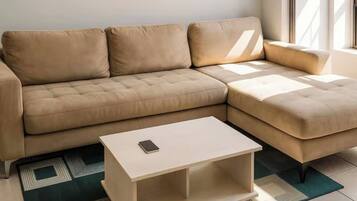 Um sofá modular com um banquinho combinando, uma pequena mesa lateral branca com um smartphone e um tapete com padrão geométrico.