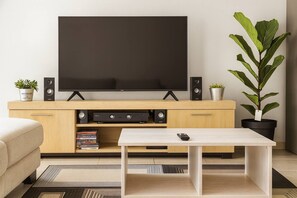 Una sala moderna con televisor de pantalla plana, mueble de entretenimiento de madera, una mesa de centro y dos plantas en macetas.