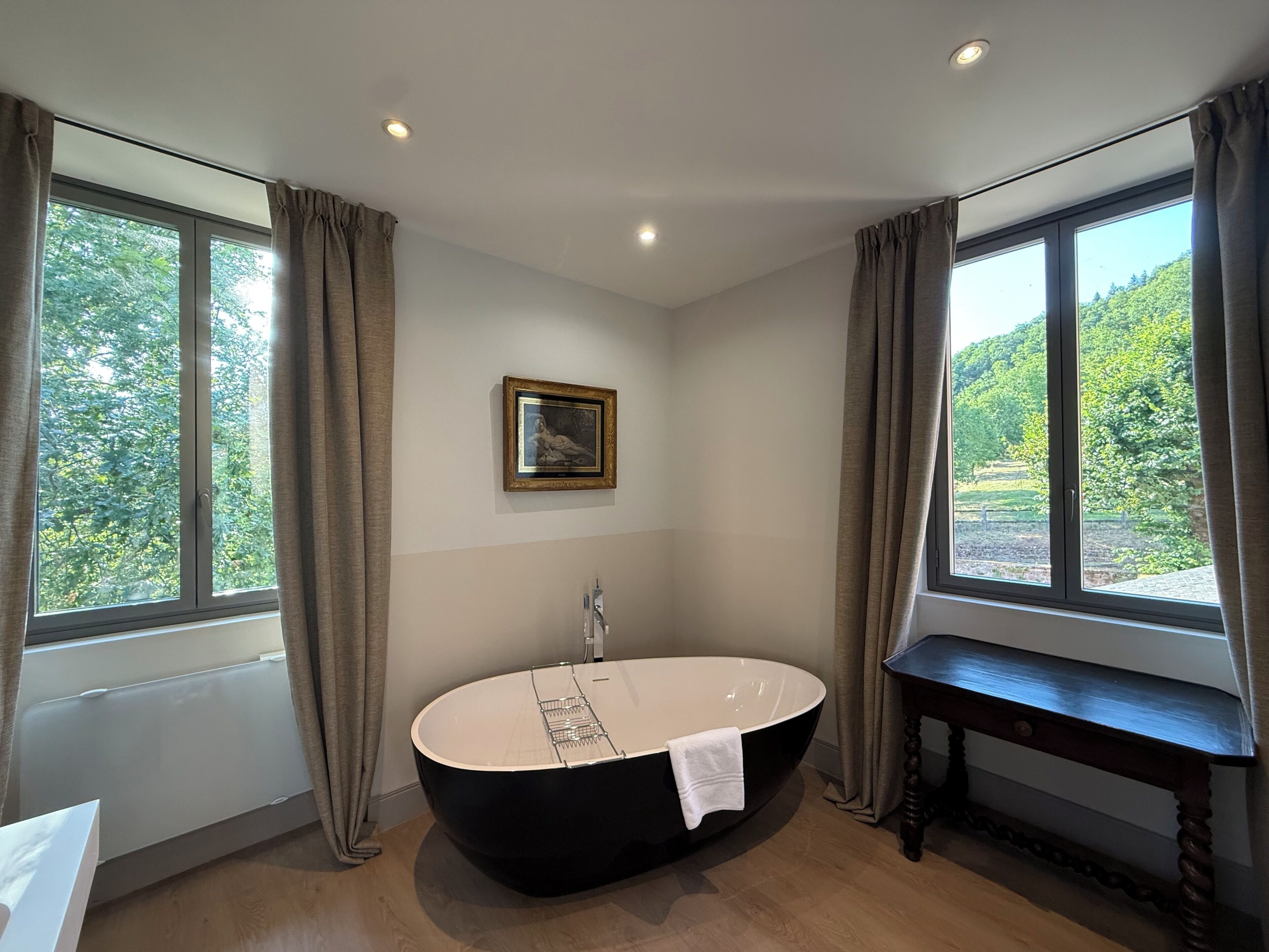 A modern bathroom with a freestanding bathtub, a wooden bench, and a framed picture on the wall.