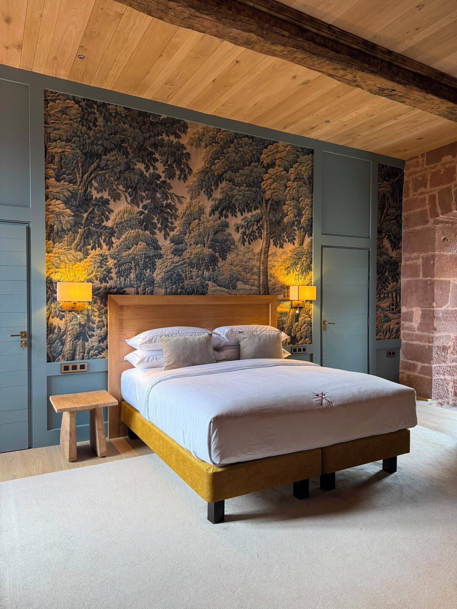 Un dormitorio con una cama de madera, una mesita de noche, un banco y una pared con un mural de un bosque.