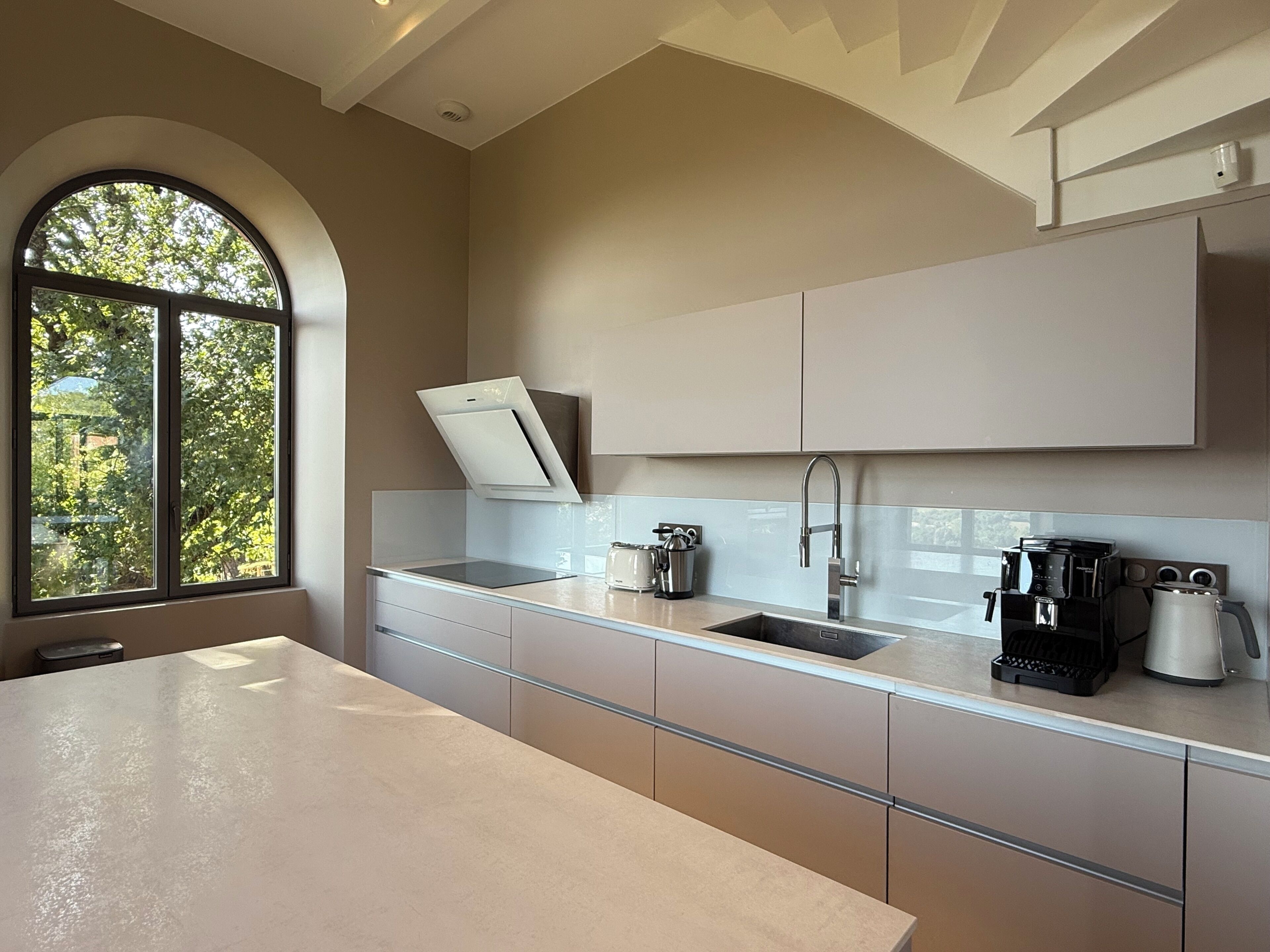 A modern kitchen with a large window, a built-in oven, and a coffee maker.