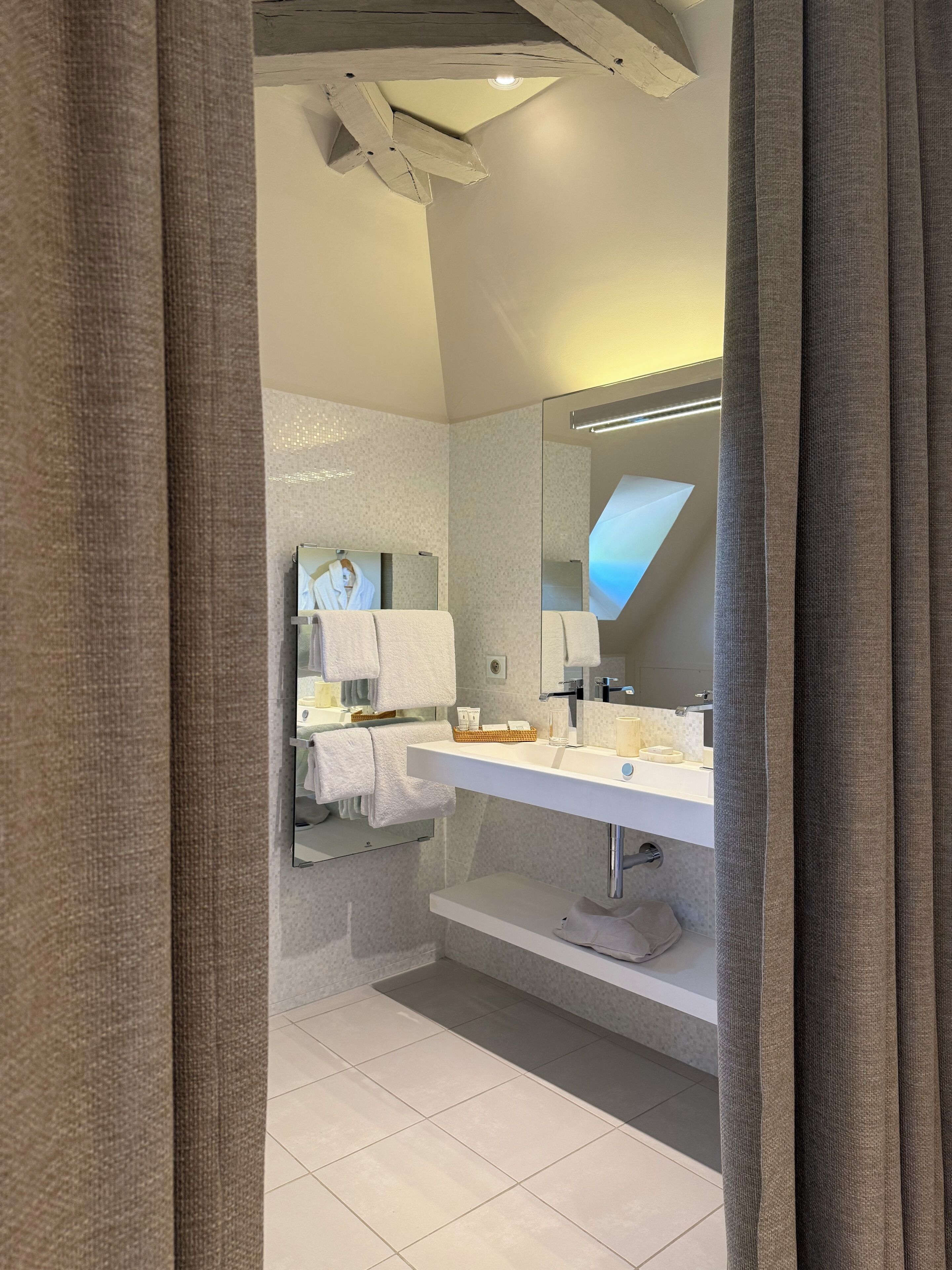 A modern bathroom with a large mirror, white tiles, and a vanity with toiletries.