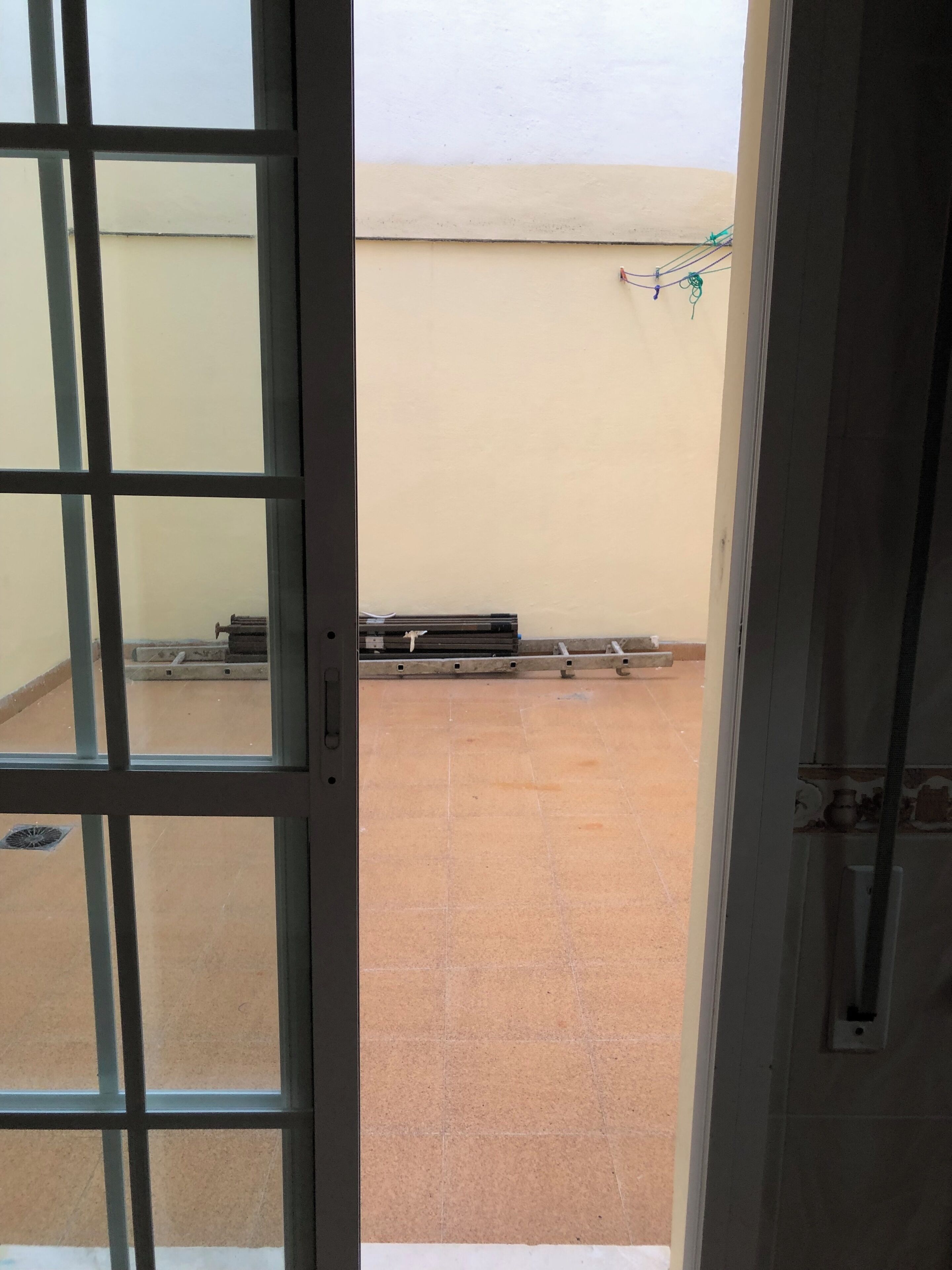 A view through a window with a metal grid, a tiled floor, and a beige wall with a white ceiling.