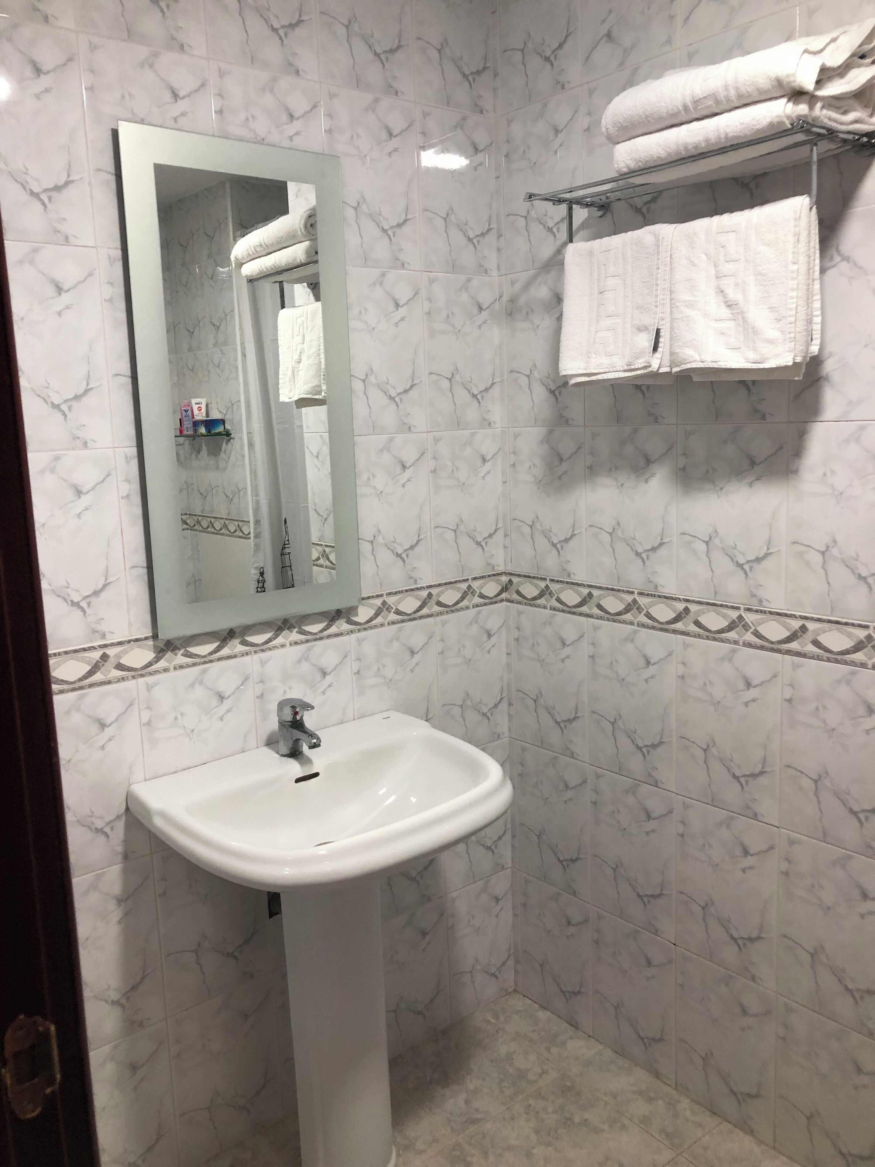 A bathroom with a white sink, a mirror, and a towel rack with folded towels.