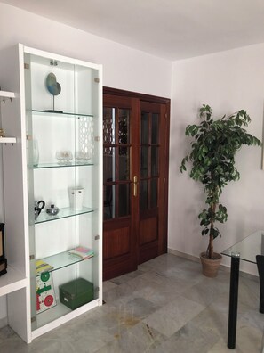 Um quarto com uma estante de vidro, porta de madeira, planta em vaso e chão de azulejos.