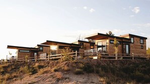 A modern wooden cabin with a deck, situated on a hillside.