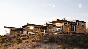 A modern wooden cabin with a deck, situated on a hillside.